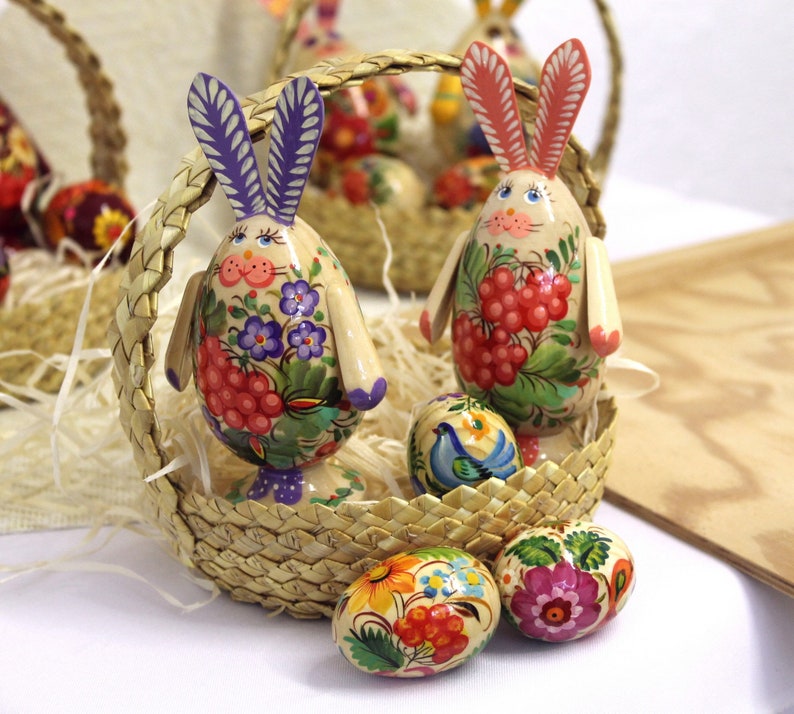 May include: A wicker basket filled with colorful, hand-painted Easter eggs and wooden bunny figurines. The eggs are decorated with floral patterns and the bunnies have intricate details.
