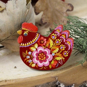 May include: A red wooden chicken ornament with a floral design painted in bright colors, including yellow, pink, and blue.