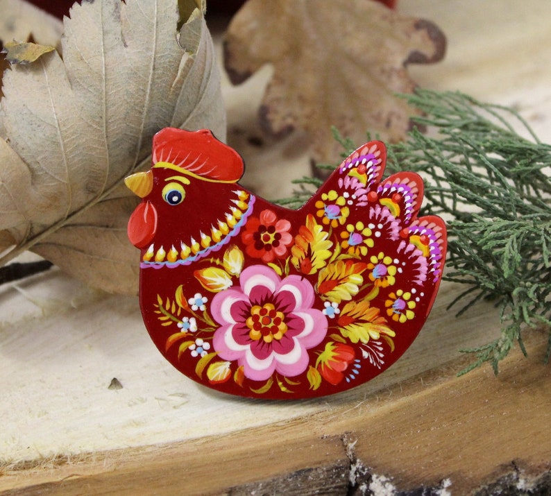 May include: A red wooden chicken ornament with a floral design painted in bright colors, including yellow, pink, and blue.