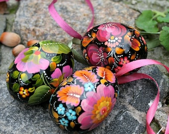 May include: Three black Easter eggs decorated with colorful floral patterns. The eggs are painted with pink, orange, yellow, and blue flowers on a black background.