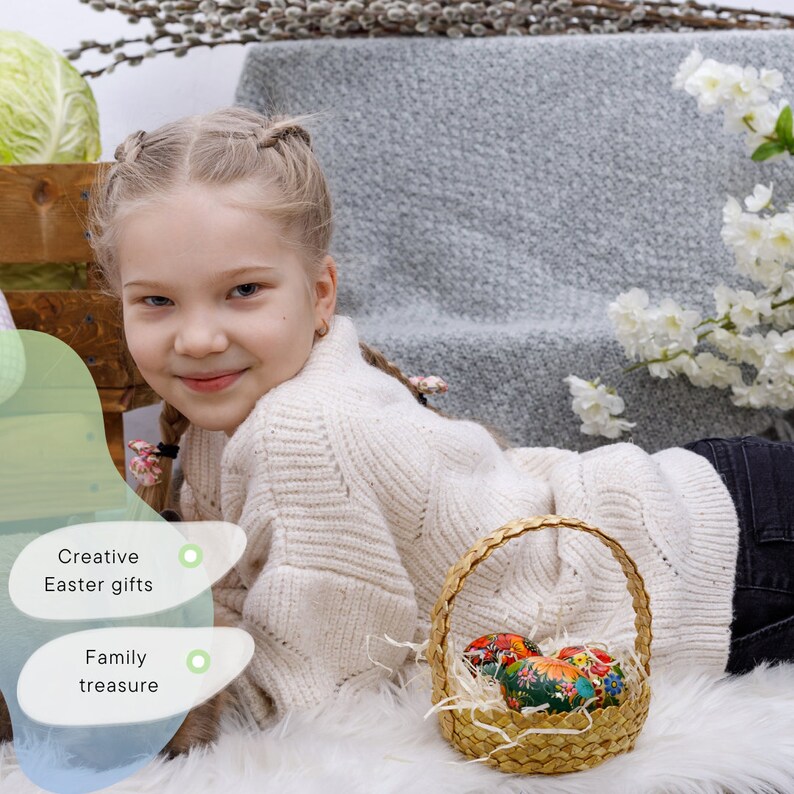 May include: A young girl with blonde braids smiles at the camera while lying on a white fluffy surface. She is holding a wicker basket filled with colorful Easter eggs. The basket is in focus, while the girl is slightly out of focus.
