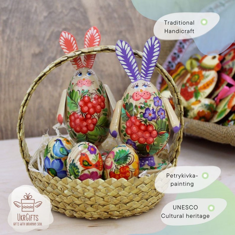 May include: Two hand-painted wooden Easter bunnies in a wicker basket with colorful eggs. The bunnies are decorated with traditional Ukrainian folk art, known as Petrykivka painting. This art form is a UNESCO Cultural Heritage.