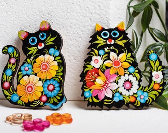May include: Two black wooden cat figurines with colorful floral designs painted on them. The cats are sitting with their tails curled around their bodies.