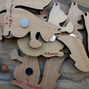 Pu&ograve; includere: Un set di magneti in legno a forma di scoiattolo con il testo "с. Петриківка ш. В" e "Л. Скляр." scritto su di essi.