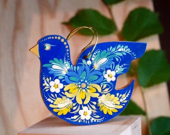 Könnte beinhalten: Ein blauer Holzvogel-Anhänger mit einem weißen und gelben Blumendesign. Der Vogel ist mit aufwendigen Details bemalt und hat eine goldene Schnur zum Aufhängen.