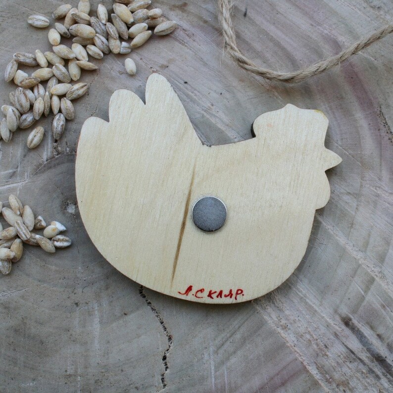 May include: Wooden chicken-shaped magnet with a silver magnet on the back. The magnet has the word "JCKAJAP" written on the bottom in red.
