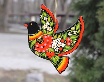 Könnte beinhalten: Ein schwarzer Holzvogel-Anhänger mit roten, weißen und grünen bemalten Blumendesigns. Der Vogel ist im Volksstilstil mit schwarzem Hintergrund und leuchtenden Farben bemalt.