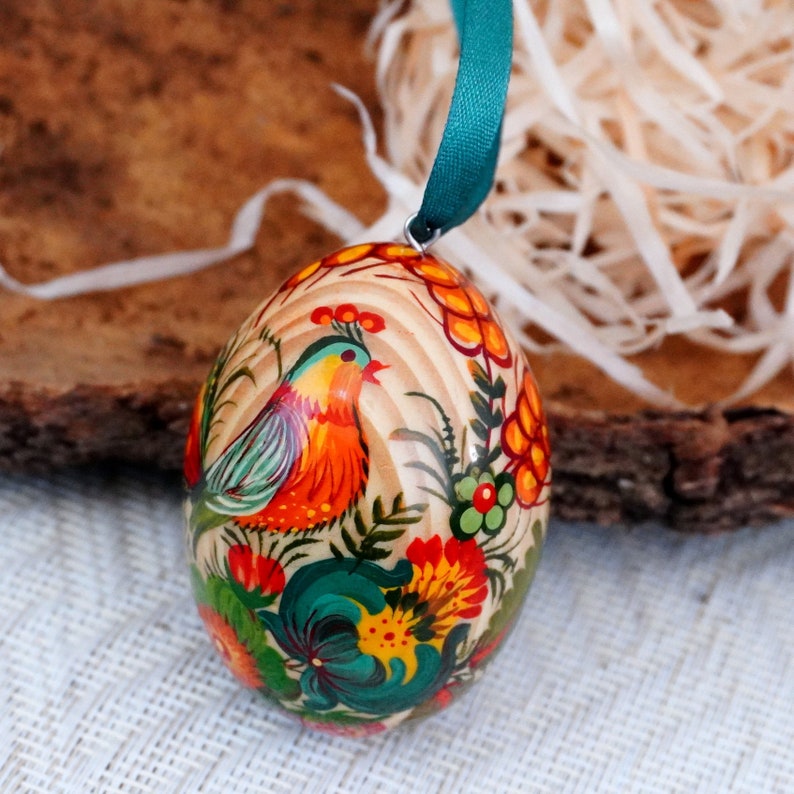 May include: A wooden Easter egg ornament with a hand-painted design featuring a colorful bird, flowers, and leaves. The egg is decorated in a traditional folk art style.