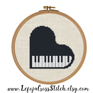 May include: A black and white cross stitch pattern of a piano shaped like a heart in a wooden embroidery hoop.