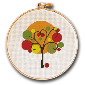 Puede incluir: Un aro de bordado de punto de cruz con un diseño de árbol abstracto de colores. El árbol tiene un tronco marrón y ramas con círculos verdes, amarillos y rojos para las hojas y los frutos. El fondo es de color naranja sólido.