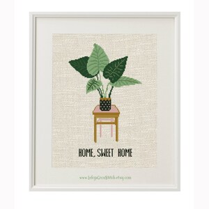 May include: Cross stitch pattern featuring a potted plant on a small table with the text "Home, Sweet Home" and the website address "www.lelojacrossstitch.etsy.com".
