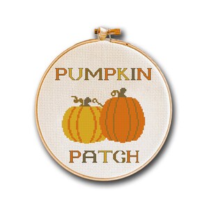 以下が含まれることがあります： 白い布地の背景を持つ丸い刺繍枠。布地には、緑色の茎と葉を持つオレンジ色のカボチャ2つが刺繍されています。カボチャの上に、茶色と黄色の文字で「PUMPKIN PATCH」と刺繍されています。