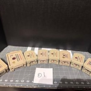 May include: A collection of beige rectangular boxes with red and black symbols and text. The boxes are arranged on a gray surface with a grid pattern. A white card with the number "10" is in the center.