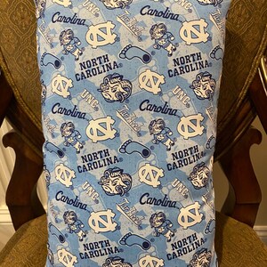 May include: A blue and white pillow with a repeating pattern of the University of North Carolina Tar Heels logo, mascot, and the words "UNC", "Carolina", and "Tar Heels".