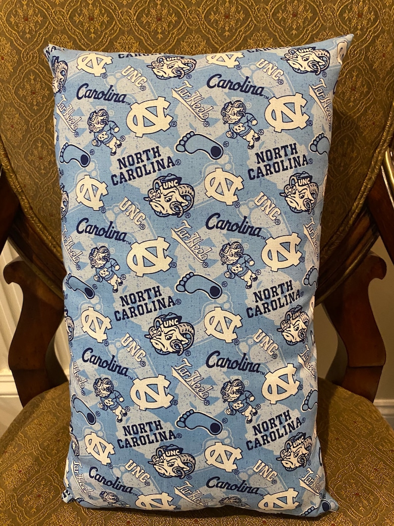 May include: A blue and white pillow with a repeating pattern of the University of North Carolina Tar Heels logo, mascot, and the words "UNC", "Carolina", and "Tar Heels".