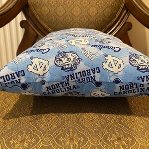 May include: A blue and white pillow with a repeating pattern of the University of North Carolina Tar Heels logo, the words "North Carolina", and "UNC".
