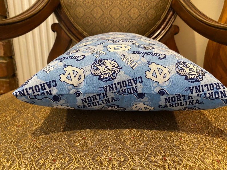 May include: A blue and white pillow with a repeating pattern of the University of North Carolina Tar Heels logo, the words "North Carolina", and "UNC".