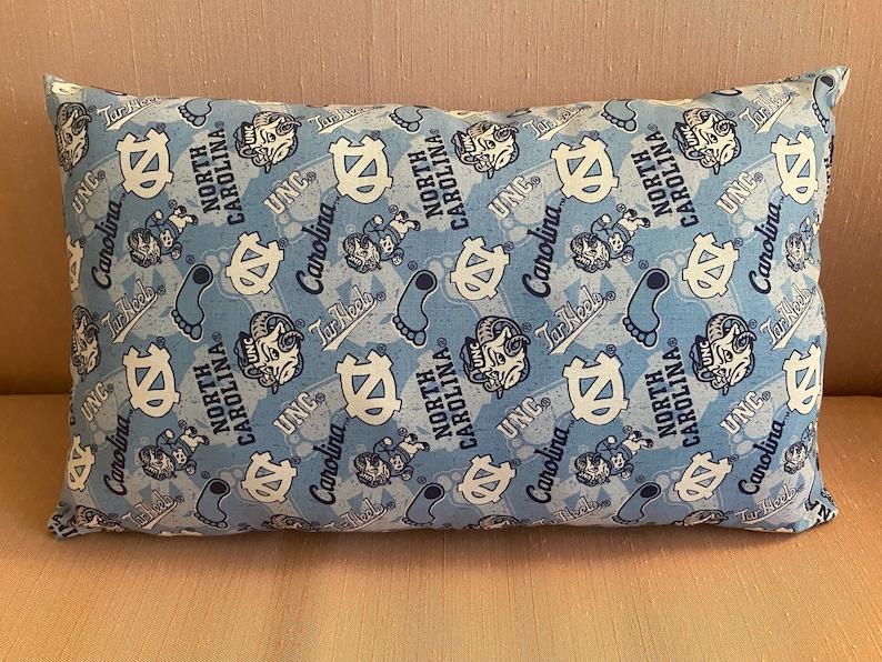 May include: A blue and white pillow with a repeating pattern of the University of North Carolina Tar Heels logo, mascot, and the words "UNC" and "North Carolina".
