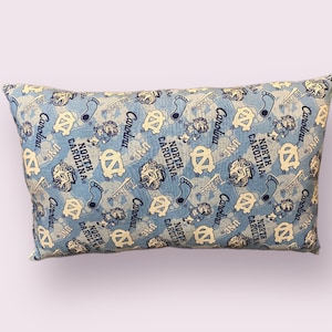 May include: A blue and white pillow with a repeating pattern of the University of North Carolina Tar Heels logo and the words "Carolina" and "North Carolina".