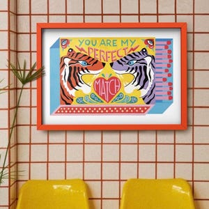 Può includere: Una stampa con cornice arancione con sfondo giallo raffigurante due illustrazioni di tigri che si fronteggiano. La stampa riporta le parole "YOU ARE MY PERFECT MATCH" e un disegno a forma di cuore. Due sedie gialle sono in primo piano.