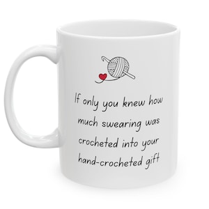 May include: A white ceramic mug featuring a black line drawing of a ball of yarn with a crochet hook and a small red heart. The text reads: If only you knew how much swearing was crocheted into your hand-crocheted gift, printed in black.