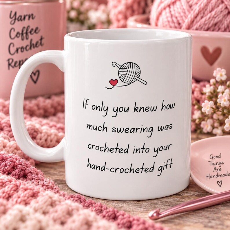 May include: A white ceramic mug featuring a black line drawing of a ball of yarn with a crochet hook and a small red heart. The text reads: If only you knew how much swearing was crocheted into your hand-crocheted gift. The mug has a handle.