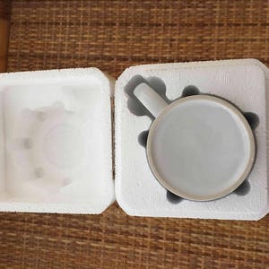 May include: A white ceramic mug with a handle, packaged in a white styrofoam box. The mug is in a protective styrofoam insert.