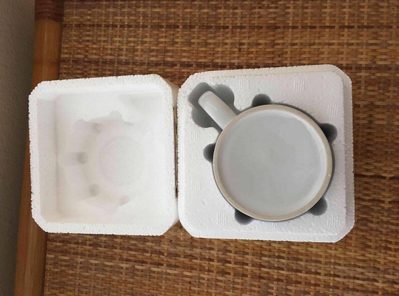 May include: A white ceramic mug with a handle, packaged in a white styrofoam box. The mug is in a protective styrofoam insert.