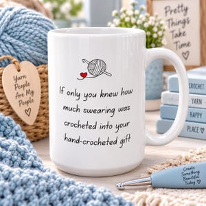 May include: A white ceramic mug featuring a black graphic of a yarn ball and crochet hook with a small red heart. The text reads: If only you knew how much swearing was crocheted into your hand-crocheted gift. The mug has a smooth finish.