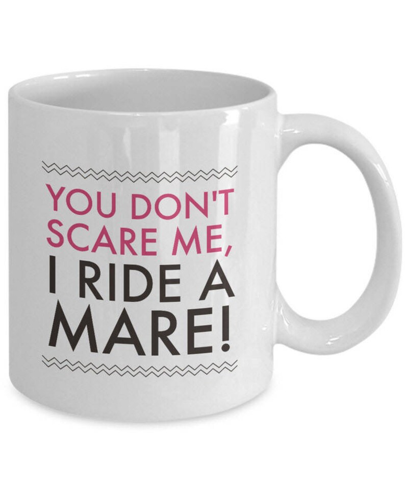 May include: White ceramic coffee mug with black text that reads "You don't scare me, I ride a mare!" The text "mare" is in pink.