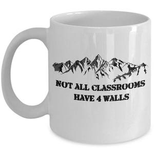 May include: White ceramic mug with a black mountain range graphic and the text "Not all classrooms have 4 walls".