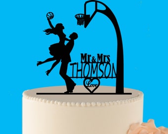 May include: Black silhouette cake topper of a couple holding a basketball with a basketball hoop and net above them. The text "Mr. & Mrs. Thomson Love" is below the couple.