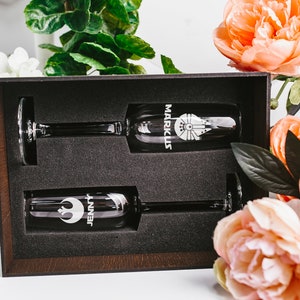 May include: Two champagne flutes in a wooden box with a black interior. The flutes are engraved with the names "Jenny" and "Mark" and a Star Wars themed design.