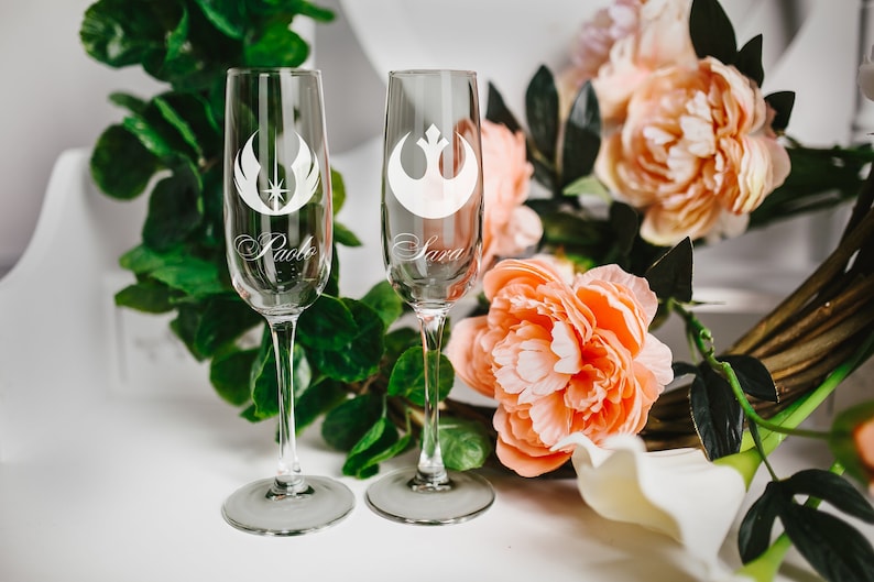 May include: Two champagne flutes with the Rebel Alliance symbol etched on them. The flutes are personalized with the names "Pablo" and "Sara".