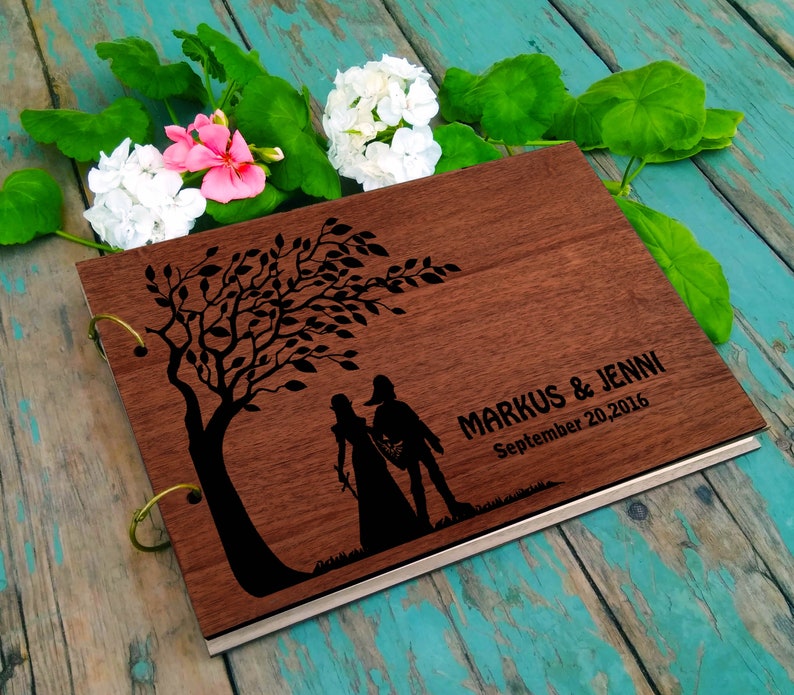May include: A wooden photo album with a silhouette of a couple walking under a tree. The album is engraved with the text "MARKUS & JENNI September 20, 2016".