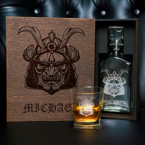 May include: A dark wooden box featuring a laser-engraved samurai helmet and the name MICHAEL, containing a glass decanter with a matching samurai engraving and the name MICHAEL, alongside a glass tumbler with the same engraving and name.