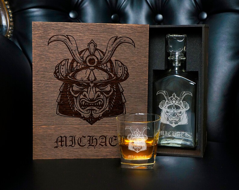 May include: A dark wooden box featuring a laser-engraved samurai helmet and the name MICHAEL, containing a glass decanter with a matching samurai engraving and the name MICHAEL, alongside a glass tumbler with the same engraving and name.