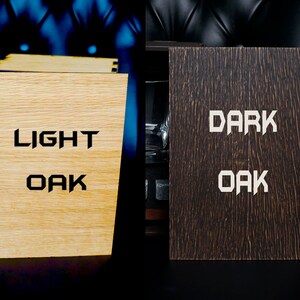 May include: Two wooden boxes with the words "LIGHT OAK" and "DARK OAK" engraved on them. The boxes are closed and sitting on a black surface.