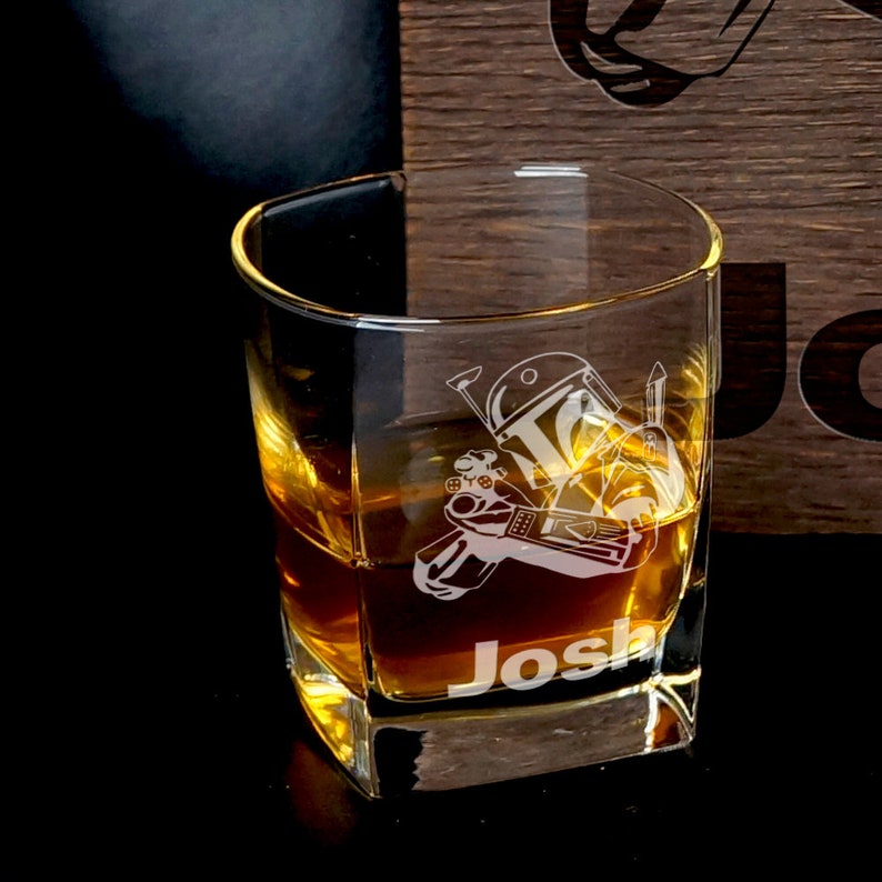 Puede incluir: Un vaso cuadrado de vidrio transparente con un dise&ntilde;o de Boba Fett y el nombre "Josh" grabado en la parte inferior. El vaso est&aacute; lleno de l&iacute;quido &aacute;mbar.