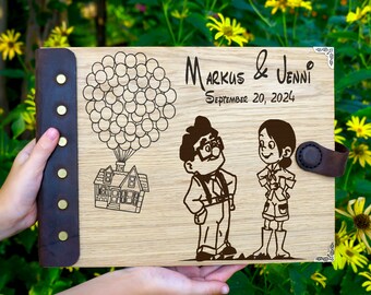 May include: A wooden guest book with a brown leather cover and metal accents. The cover features an engraved design of a house with balloons, a couple, and the text "Markus & Jenni September 20, 2024".