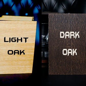 May include: Two wooden boxes with the words "LIGHT OAK" and "DARK OAK" engraved on them. The boxes are closed and sitting on a black surface.