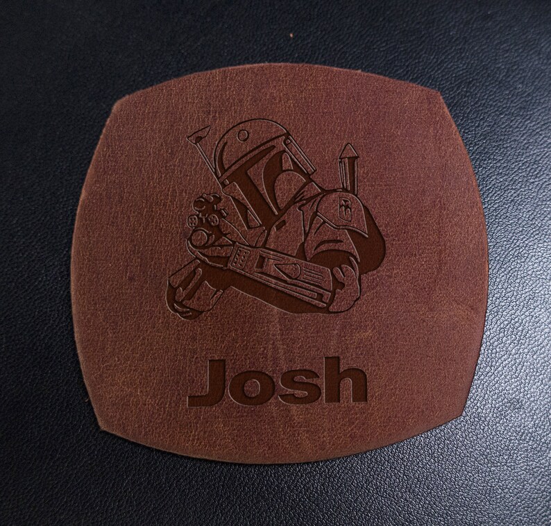 Puede incluir: Posavasos de cuero marr&oacute;n con una imagen grabada con l&aacute;ser de un personaje de Star Wars, Boba Fett, y el nombre "Josh".
