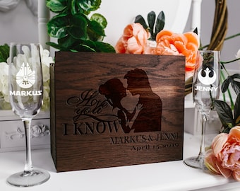 Può includere: Una scatola di legno con un design inciso a laser di una coppia che si abbraccia. Il testo "I love you I KNOW" è inciso sulla scatola. La scatola è decorata con due flute da champagne, una con un design di Millennium Falcon di Star Wars e l'altra con un simbolo dell'Alleanza Ribelle. Le flute sono incise con i nomi "Markus" e "Jenny". La scatola ha anche i nomi "Markus & Jenny" e la data "April 15, 2019" incisi.