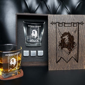 May include: Two engraved whiskey glasses with a lion crest design, in a wooden box with a matching engraved lion crest design. The box also includes four ice cubes.
