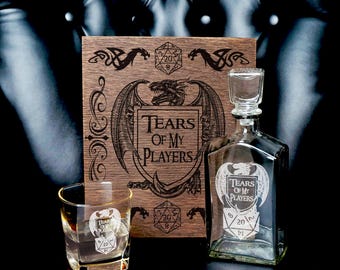 May include: A clear glass decanter and a matching rocks glass, both etched with a dragon and a 20-sided die graphic featuring the text Tears of My Players. Behind them stands a rectangular wooden board with matching laser-engraved artwork.