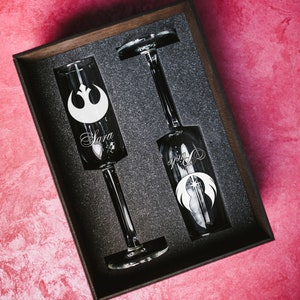 May include: Two champagne flutes in a black box with a black foam interior. The flutes are engraved with the Star Wars Rebel Alliance symbol and the names "Sara" and "Phil".