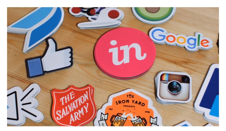 May include: A collection of colorful stickers featuring various logos, including Facebook, Instagram, Google, LinkedIn, and The Salvation Army. The stickers are arranged on a wooden surface.