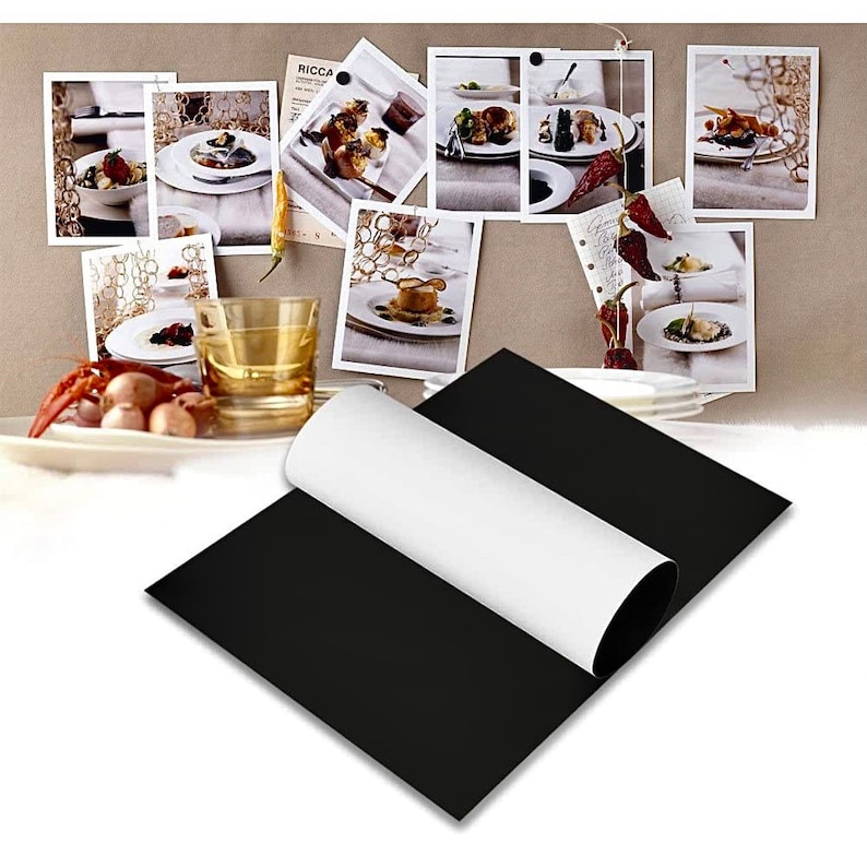 May include: A black magnetic sheet with a white backing. The sheet is rolled up and partially unrolled, revealing the white backing. The sheet is on a table with a glass of water and a plate of food.