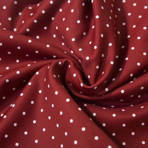 May include: Red fabric with white polka dots. The fabric is folded and textured.