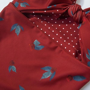 May include: A red swimsuit with a white polka dot pattern on the inside. The swimsuit has a knotted detail at the top and a floral print.
